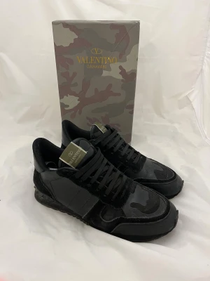 Valentino Garavani Rockrunner sneakers - Snygga svarta Valentino Garavani Rockrunner sneakers med coola camouflagedetaljer. Skorna har en mix av skinn och mocka, svarta snören och en klassisk rund tå. Perfekta för dig som vill ha en exklusiv och trendig look.