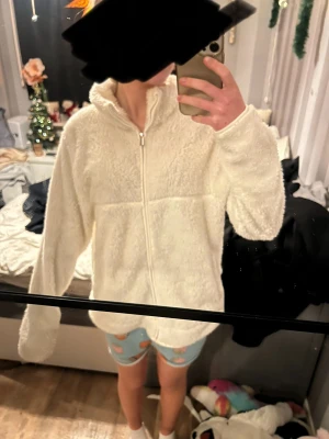 Vit teddyjacka från 157 - Mysig vit teddyjacka från 157 i storlek M. Jackan har en hög krage, dragkedja framtill och långärmade ärmar. Den är fluffig och har en loose passform som ger en chill vibe. Perfekt för kalla dagar när du vill vara både bekväm och snygg.