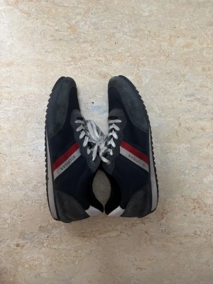 Tommy Hilfiger Essential Mesh Runner - Snygga sneakers från Tommy Hilfiger i mörkblått med grå mockadetaljer och vit/röd rand på sidan. Skorna har vit snörning, platt sula och rund tå. Materialmix av mesh och mocka ger en sportig vibe. Perfekt för dig som gillar klassisk streetstil med en twist.
