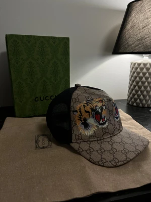Gucci keps tiger - Snygg Gucci keps i beige och brunt, mesh i svart baktill och broderade tigrar framtill. Låda samt dustbag följer med. 