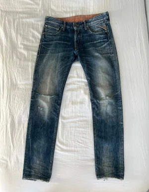 Replay Jeans Straight Fit - Ett par straight jeans med slitningar från Replay, i storlek 30/34. Riktigt snygga med denimslitage och tydliga ”whiskers” (veckmönster). 100% bomull.   Eftersom detta är en second hand-vara kan det finnas små brister, men jag har inte märkt några och därför inte nämnt några. Skicka gärna ett meddelande om du har frågor eller vill föreslå ett pris.  Mått (+/-1cm) Midja: 44 Innerbenslängd: 83 Ytterbenslängd: 104 Midjehöjd: 24 Lår: 21 Öppning: 17