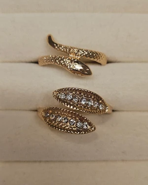 Guldiga ringar med ormdesign och stenar - Två coola guldiga ringar, en med detaljerad ormdesign och en med glittrande stenar på två spetsiga ändar. Perfekt för dig som gillar unika och trendiga smycken med lite edge. Säljs tillsammans!✨️🫶