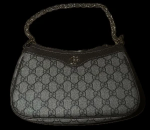 Gucci väska - ‼️Kommer med Original box och förpackning‼️Snygg axelväska från Gucci med klassiskt GG-mönster i beige och mörkbrunt. Väskan har en silverfärgad kedja som axelrem och detaljer i brunt skinn. Perfekt storlek för det viktigaste och har dragkedja upptill. Ikonisk logga framtill.