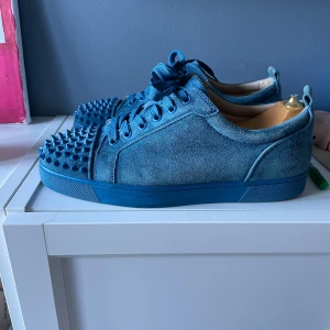 Christian Louboutin sneakers  - Säljer ett par blå sneakers från Christian Louboutin i mocka med coola nitar på tån och klassisk röd sula. Skorna har snörning och en chunky vibe som sticker ut. Perfekta för dig som vill ha något unikt och vågat i garderoben.