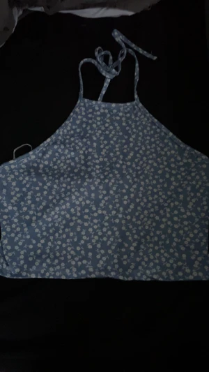 Blommig blå linnetopp med knytband - Blå topp med vita små blommor och knytband i nacken. Croppad passform. Är en lös tråd längst ut på ena snöret. Stl M från SHEIN.