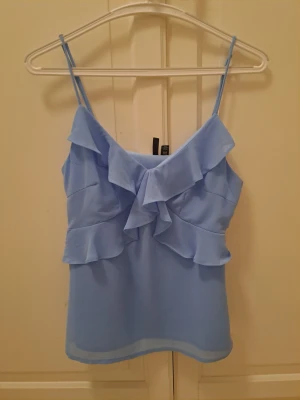 Ljusblå volangtop från Vero Moda - Ljusblå linnetopp från Vero Moda med tunna axelband och volang. 