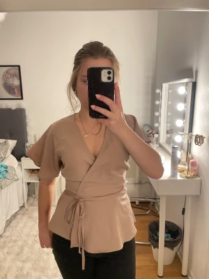 Beige omlottblus från Bubbleroom - Jättefin omlott blus från bubbleroom. Jag skulle säga att den första bilden är mest lik färgen i verkligheten