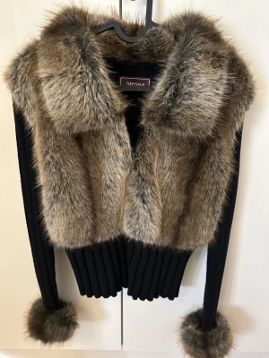 Svart pälsjacka från Alessa - Säljer en svart pälsjacka från Alessa med fluffiga bruna och grå pälsdetaljer på krage, framstycke och ärmslut. Jackan har ribbstickad kropp och ärmar, samt dragkedja framtill. Perfekt för dig som vill ha en unik och trendig look. Helt nytt skick aldrig använt 