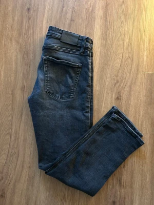  jeans från Jack & Jones - Snygga mörkblå jeans från Jack & Jones med klassisk femficksdesign och bekväm passform. Jeansen har raka ben och är tillverkade i stretchig bomullsdenim för extra komfort. Perfekta för dig som gillar en stilren look.