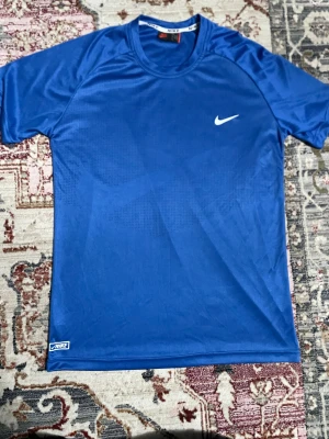 Blå Nike t-shirt  - Snygg blå t-shirt från Nike i storlek L. Tillverkad i lätt och ventilerande polyester, perfekt för träning. Klassisk rund halsringning och korta ärmar. Diskret Nike-logga på bröstet och nacken för en sportig look.