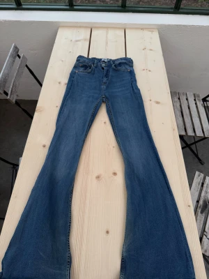 Blå bootcut jeans från 157 - Snygga blå jeans från 157 med klassisk femficksdesign och bootcut-ben. Jeansen har hög midja och är tillverkade i mjukt denimtyg med lätt slitning. Perfekta för dig som gillar retrovibbar och vill ha en bekväm passform med lite utsvängda ben.