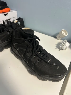 Svarta Nike sneakers med chunky sula - Nike sneakers i helsvart med chunky, bubblig sula och snörning. Ovandelen är i syntetmaterial med detaljer i plast och textil. Rund tå och platt sula ger en sportig vibe. Perfekt för dig som gillar streetwear och vill ha en clean look.