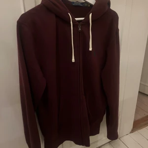 Vinröd zip från Polo Ralph Lauren - Säljer en vinröd zip hoodie från Polo Ralph Lauren i storlek M. Tröjan har huva med vita snören, dragkedja framtill och klassisk logga broderad på bröstet. Perfekt skick. Använd endast ett fåtal gånger. Nypris 1800kr. 