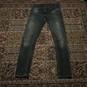 Svarta skinny jeans från Nudie Jeans - Säljer ett par svarta  jeans från Nudie Jeans i storlek 25/32. Jeansen har klassisk femficksdesign, dragkedja och knapp framtill samt diskreta slitningar för en cool look. Perfekta om du gillar en bra passform och stilren vibe.