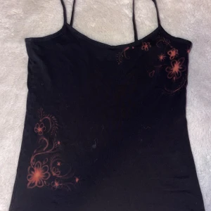 Svart linnetopp med blommigt mönster - Svart linnetopp med smala axelband. Har själv blekt ett blommigt mönster på ena sidan och vid bröstet. Toppen har en figurnära passform och är tillverkad i mjukt bomullsmaterial. Perfekt för dig som gillar detaljer och vill sticka ut lite extra.