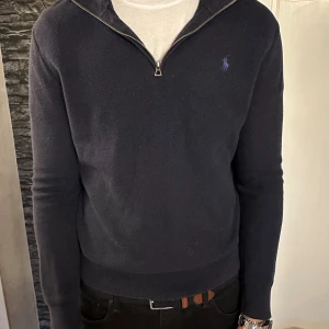 Mörkblå half zip tröja Polo Ralph Lauren - Säljer en mörkblå långärmad tröja från Polo Ralph Lauren med half zip och broderad logga på bröstet. Tröjan är i mjuk bomull och har en klassisk passform med ribbade muddar och krage. Perfekt för lager-på-lager och snygg till jeans. Köpt på Best of brands, nypris: 2500kr