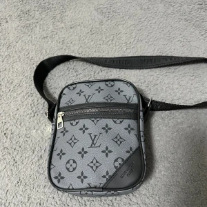 Axelväska  - En fin grå axelväska, med fina mönster på! Den har även en fin text på själva bandet🔥Helt oanvänd! 