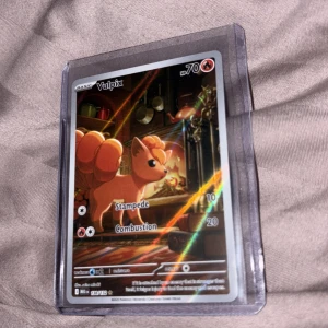 Vulpix - Cool Pokémon-samlarbild med Vulpix i ett mysigt kök. Kortet har glansig finish och visar Vulpix med sina attacker Stampede och Combustion. Perfekt för dig som älskar Pokémon och vill utöka din samling med en unik och snygg kort!