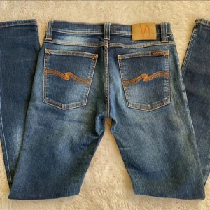 Nudie jeans ”Tight Long John” W28 L34 - hej säljer min Nudie jeans i storleken W28 L34. Längden på jeansen kan va kortare än L34. Modell Tight Long John. Inga defekter alls. Nypris: ca 1800 kr | Mitt pris: 599 kr  	•	Bredd (midja): 38 cm 	•	benlängd: 73 cm 	•	Längd : 97 cm Skriv vid minsta lilla fundering eller om du inte håller med om priset!