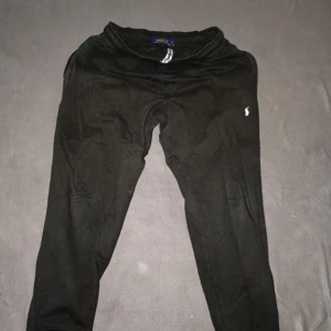 Svarta mjukisbyxor från Polo Ralph Lauren - Svarta mjukisbyxor från Polo Ralph Lauren med klassisk logga broderad på vänster höft. Byxorna har resår i midjan och är tillverkade i mjukt bomullsmaterial, perfekta för chill dagar eller träning.