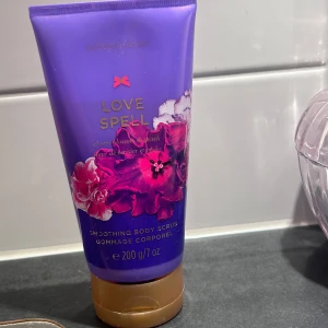 Victoria's Secret Love Spell Body Scrub - Love Spell Smoothing Body Scrub från Victoria's Secret med doft av körsbärsblom och persika. Tuben är lila med guldigt lock och dekorerad med rosa och lila blommor. Innehåller 200 g.