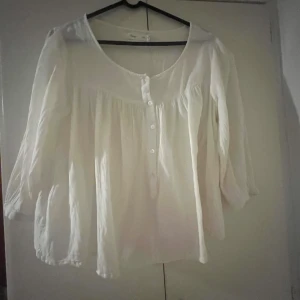 Vit blus från Vintage, storlek M - Luftig vit blus från Vintage i storlek M. Blusen har rund halsringning, knappar framtill och långa ärmar. Den är tillverkad i ett tunt, lätt material och har en lös passform med fina rynkade detaljer både fram och bak.