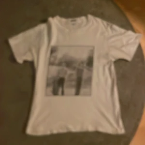 Vit t-shirt med tryck från Fiore - Snygg vit t-shirt från Fiore i storlek XS med ett stort svartvitt fototryck på framsidan. Klassisk rund hals och korta ärmar. Perfekt för dig som gillar golf eller bara vill ha en Feet tröja.