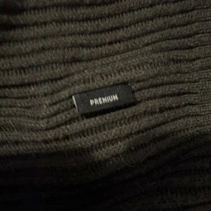 Svart ribbad half zip från Jack & Jones - Mörk, ribbstickad tröja från Jack & Jones med half zip-dragkedja och hög krage. Tröjan är långärmad och har en stilren look med diskret 'PREMIUM'-märke. Perfekt för dig som gillar enkel och snygg stil.