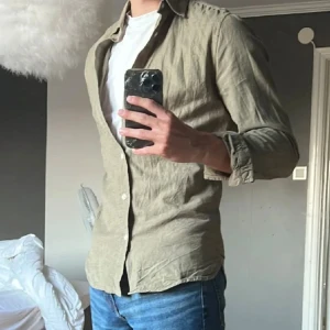 Grön Dobber skjorta  - Säljer en stilren skjorta från Dobber i en riktigt snygg grön/olivgrön färg. Storlek S men passar även M. Är i mycket bra skick och knappt använd. Tveka ej att höra av dig vid intresse!