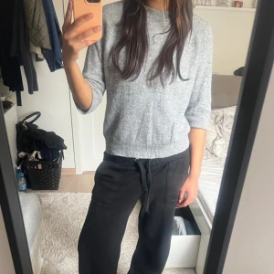 Grå stickad tröja med trekvartsärm - Mysig grå stickad tröja med rund hals och trekvartsärmar. Tröjan har en enkel, clean look och är lite croppad i modellen. Perfekt för dig som gillar en chill och stilren vibe. Passar till både jeans och mjukisbyxor.
