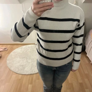 Vit polotröja med svarta ränder - Säljer en ribbad vit polotröja med svarta horisontella ränder. Tröjan har lång ärm och hög krage som ger en clean och chill vibe. Materialet är stickat och passar perfekt när man vill vara både bekväm och snygg. Fråga om du vill ha fler bilder!
