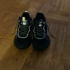 Svarta chunky sneakers med vita detaljer - Svarta chunky sneakers med grov sula och vita kontrastdetaljer. Skorna har snörning, mesh- och syntetmaterial samt orangea detaljer på plösen och hälen. Perfekta för dig som gillar streetstyle och vill sticka ut med en modern look.