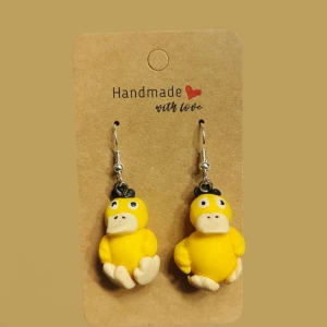 Psyduck pokemon örhängen - Supergulliga handgjorda örhängen med Psyduck från Pokémon! De är formade som små figurer i klargult och beige, med svarta detaljer på huvudet. Perfekta för dig som älskar unika accessoarer och vill sticka ut med något lekfullt.