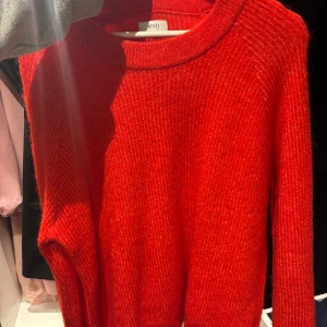 Röd stickad tröja från Envii - Säljer en snygg röd stickad tröja från Envii med rund hals och långa ärmar. Tröjan har en ribbad struktur som ger en cool och trendig look, perfekt för att hålla dig varm under kyliga dagar. Passar dig som gillar färgstarka plagg.