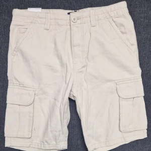 Beige cargoshorts 157 – trendig streetwear-look (S) - Fräscha beige cargoshorts från 157 i storlek S. Aldrig använda – i toppskick! Klassisk modell med sidfickor och avslappnad passform som passar perfekt till sommaren, strand, festival eller vardagsoutfits. Mjukt och slitstarkt tyg med skön känsla. Enkla att matcha med t-shirt, linne eller hoodie.   Snabb leverans  Öppen för bud  Storlek: S  Skick: Mycket bra (använda 1–2 gånger)  Material: Bomullsmix