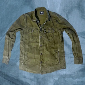 Camouflage overshirt från Abercrombie - Asfet overshirt från Abercrombie & Fitch i grönt camouflage-mönster. Skjortan har klassisk krage, två bröstfickor med knappar och långa ärmar. Tillverkad i mjuk bomull med detaljerade sömmar och knappstängning framtill. Perfekt plagg för våren/hösten . Kan tänka mig gå ner i pris vid snabb affär! Ha de bra! // Gidlöfs