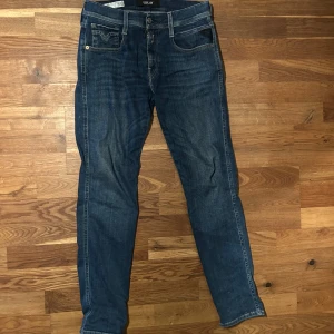 Replay Anbass jeans blå, stl 29/30 - Snygga blå Replay Anbass jeans i klassisk femficksmodell med ljusa sömmar och cool detalj på bakfickan. Jeansen har dragkedja och knappstängning, samt en slim passform som sitter riktigt bra. Perfekt för dig som gillar stilrena och bekväma jeans. Köpta på Jeansbolaget (Pris går att diskutera vid snabb affär)