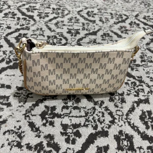 Beige axelväska från Huomengmilan - Snygg beige axelväska med grått rutigt M-mönster och guldfärgad logga. Väskan har dragkedja upptill, guldfärgade detaljer och ett rymligt fack med innerficka. Perfekt storlek för det viktigaste och cool design som sticker ut.