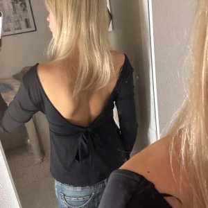 Svart topp med öppen rygg och knyt - Svart långärmad topp med djup v-ringning framtill och öppen rygg med snygg knyt-detalj.