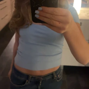 Ljusblå croppad topp - Säljer en ljusblå croppad topp med korta ärmar. Enkel och stilren design som passar perfekt till jeans eller kjol. Mjuk och skön att ha på sig.