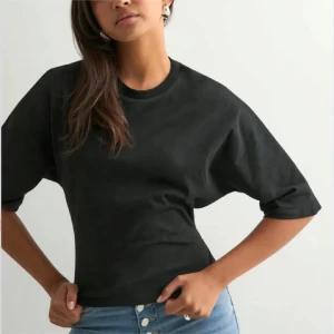 Svart  topp med knyt i ryggen, nelly - Svart croppad topp med halvlånga ärmar och öppen rygg. Toppen har en snygg knytning med stor rosett baktill som ger en unik look. Tillverkad i ett mjukt bomullstyg och passar perfekt till jeans eller kjol.