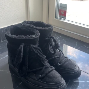 Svarta Inuikii boots med snörning - Svarta boots från Inuikii med mysigt foder. Skorna har en rund tå, platt sula och är tillverkade i mocka och skinn. Perfekta för kalla dagar med sin varma insida och coola look. De är i fint använt skick, smuts som går att tvätta bort. En defekt är skosnörena som har gått upp lite grann längst fram.