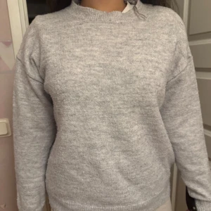 Grå stickad tröja från Gina Tricot - Mysig grå stickad tröja från Gina Tricot med rund hals och ribbade muddar vid hals, ärmslut och nederkant. Tröjan har en enkel, klassisk design och är långärmad, perfekt för kyliga dagar. Passar dig som gillar en clean och chill stil.