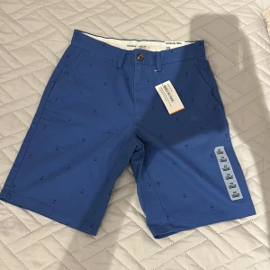 Blå shorts med ankarmönster Old Navy - Snygga blå shorts från Old Navy med slim passform och ankarmönster över hela tyget. De har klassisk knappstängning, bälteshällor och sidofickor. Materialet är mjuk bomull med inbyggd stretch för extra komfort. Perfekta för sommarens alla äventyr.