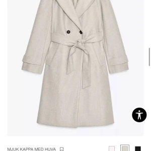 Beige kappa med huva från Zara - Stilren beige kappa från Zara med huva, knytskärp i midjan och dubbelknäppning framtill. Långa ärmar med dekorativa knappar vid ärmslut och bred krage. Perfekt för kyligare dagar och ger en klassisk looks. Storlek Xs jätte fin kappa har använt den fem gånger jätte skön och varm funkar jätte bra att använda den på vintern eller hösten. 