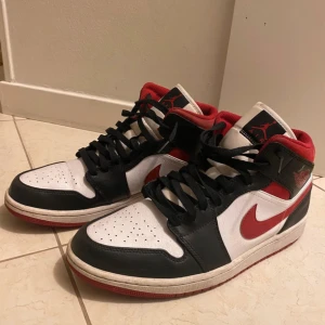 Nike Air Jordan 1 Mid Svart/Röd/Vit - Nike Air Jordan 1 Mid sneakers i svart, rött och vitt med klassisk Jordan-logga på plösen och sidan. Skorna har snörning, perforerad tå och röd insida. Storlek US 11/ EU 45. Använt 1 gång helt nya och fräscha- se bilderna. Äkta!!
