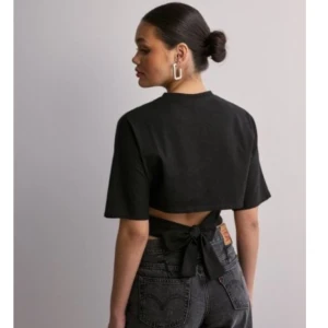 Svart croppad bolerotopp med knyt - Svart croppad bolerotopp med korta ärmar och snygg knytning i ryggen. Toppen har en enkel och stilren design som ger en cool vibe. Perfekt att matcha med höga jeans eller kjol för en trendig look.