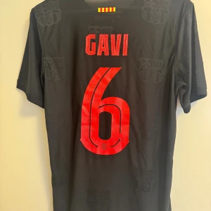 FC Barcelona Gavi #6 svart matchtröja - Snygg svart unik FC Barcelona fotbollströja från Nike med Gavi och nummer 6 på ryggen. Tröjan har röda detaljer, klubbmärke, Nike-logga och Spotify-logga på bröstet. Tillverkad i lätt och ventilerande material, perfekt för match eller träning.