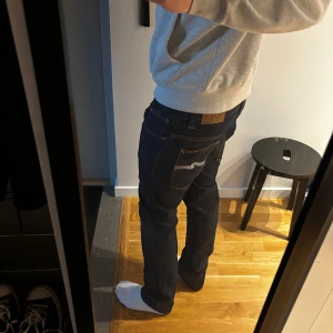Mörkblå Nudie Jeans, rak modell - Säljer ett par mörkblå jeans från Nudie Jeans i rak passform. Jeansen är tillverkade av 100% ekologisk bomull och har klassiska kontrastsömmar samt Nudie-logga på bakfickan. Snygg och tidlös modell som passar till det mesta. Jeansen är nästan helt oanvända. Storlek: W34 L32. Skriv om du har funderingar😁