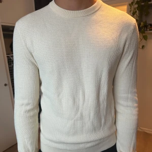 Vit stickad tröja från Riley - Säljer en stilren vit stickad tröja från Riley. Tröjan har rund halsringning, lång ärm och ett diskret strukturerat mönster i materialet. Perfekt för dig som gillar en clean och klassisk look. Köpt på Åhléns, nypris 800kr